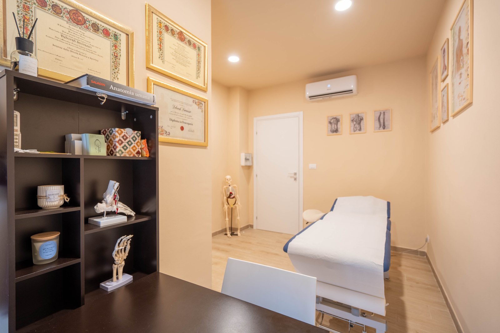 Sala osteopatia vista dalla scrivania: libreria, lettino e porta d’ingresso